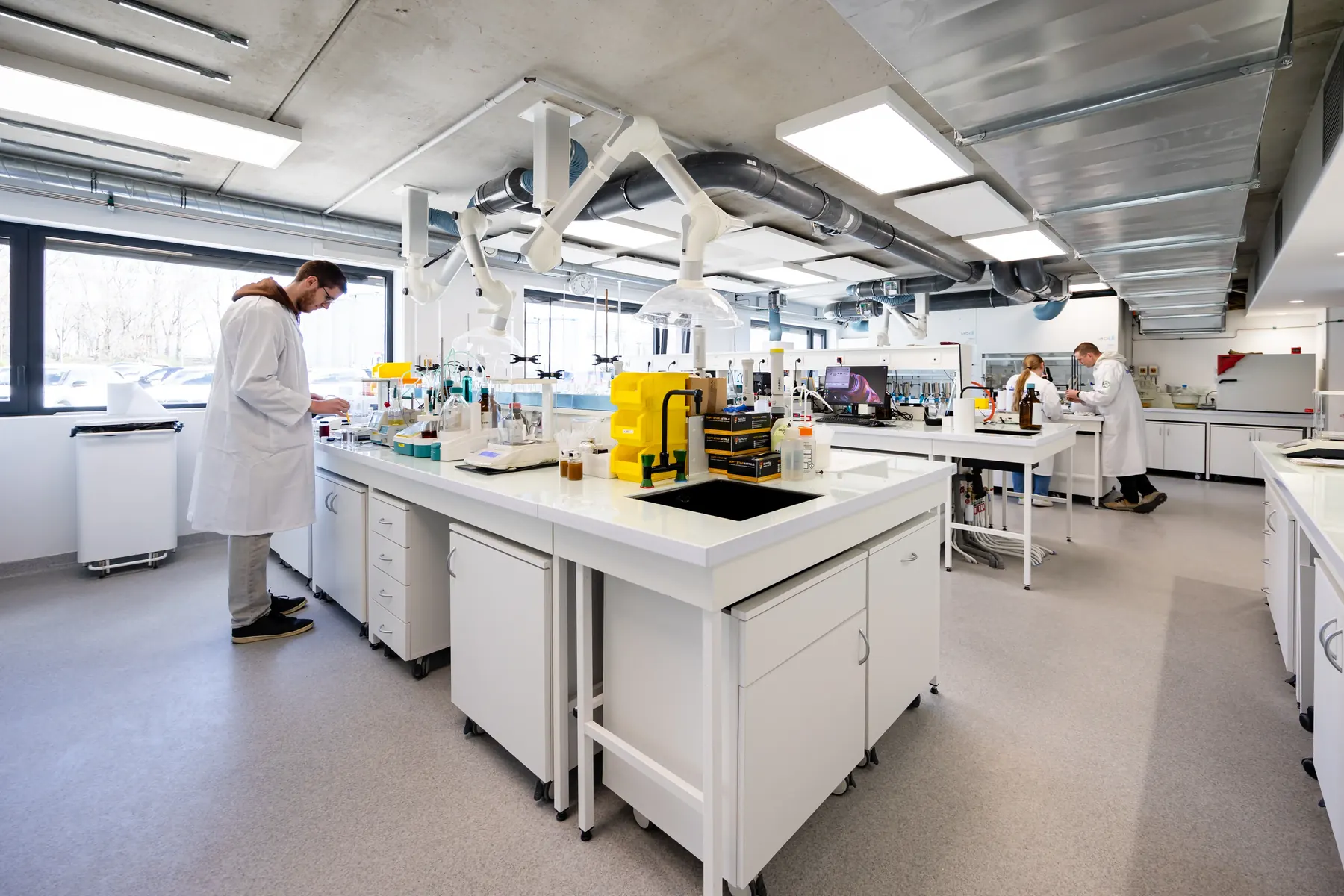 Laboratoire ou plateau technique : plusieurs techniciens à leurs postes, mobilier roulant blanc et sol de circulation professionnel